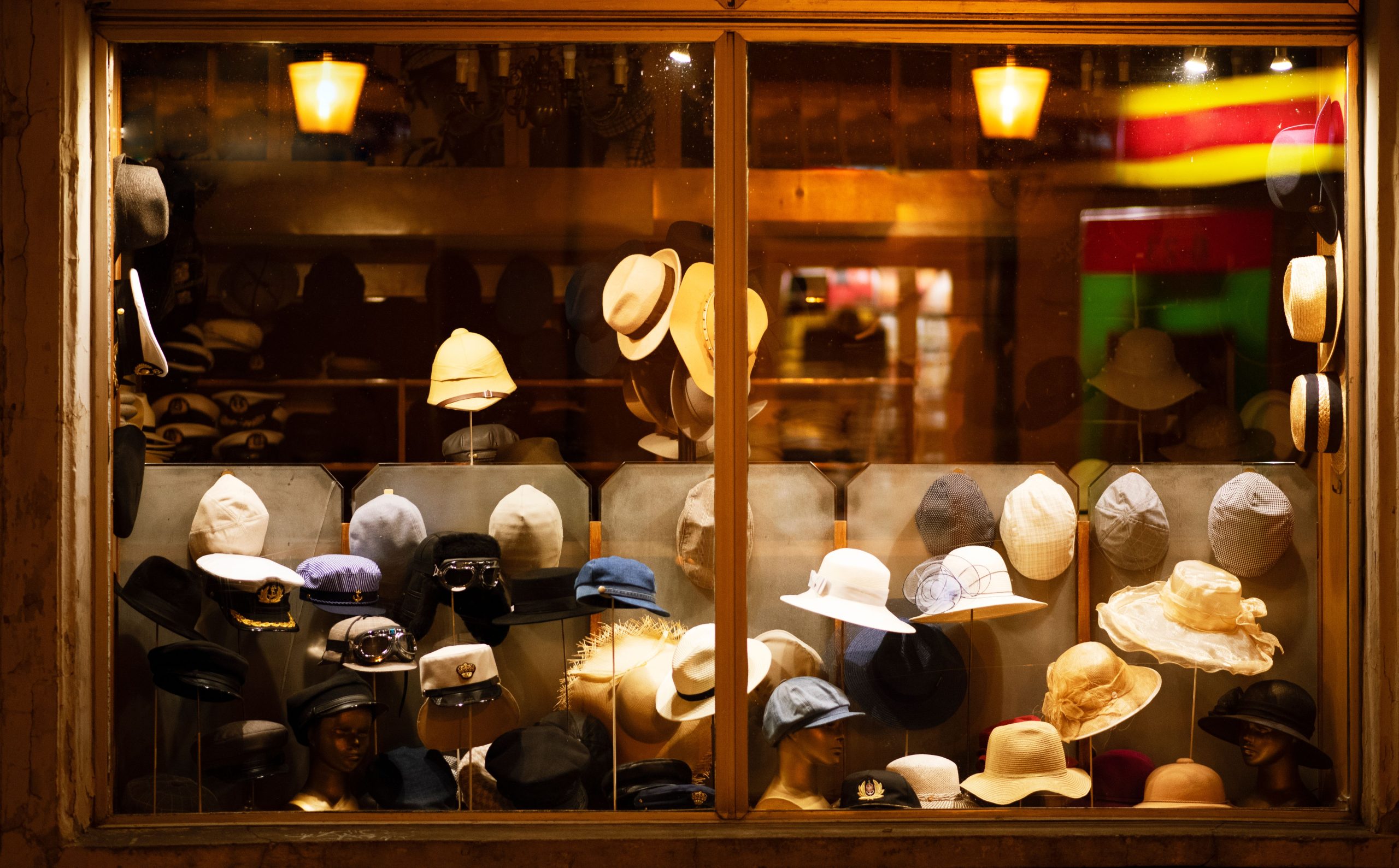 A colorful assortment of hats showcased in a warmly lit store window during nighttime.